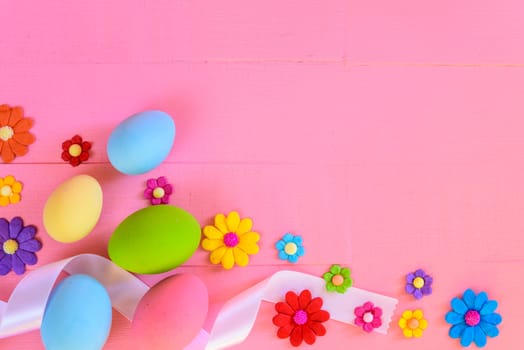 Easter eggs with colorful paper flowers on bright pink wooden background.