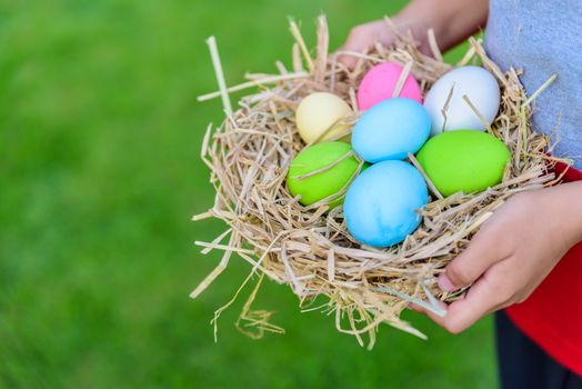 A kid holding Colorful of Easter eggs in nest on grass green background.