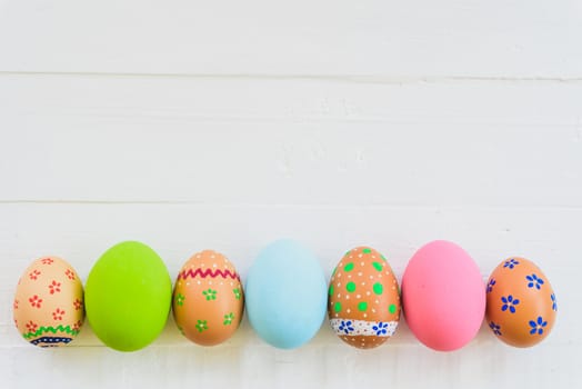 Happy easter! Row Colorful Easter eggs with colorful paper flowers on white wooden background.