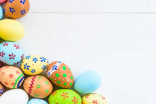 Happy easter! Row Colorful Easter eggs with colorful paper flowers on white wooden background.