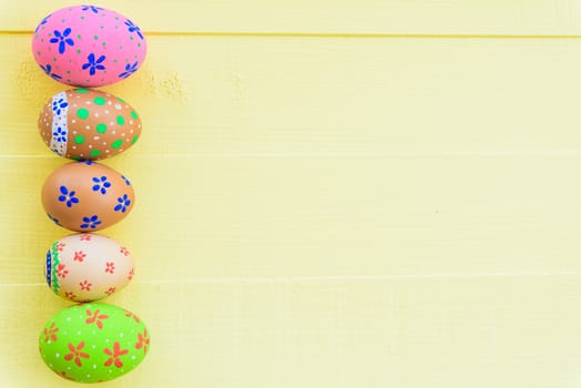 Happy easter! Row Colorful Easter eggs with colorful paper flowers on bright yellow wooden background.
