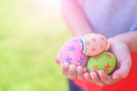 Happy easter! Close up of little kid holding colorful Easter eggs on green grass field background.