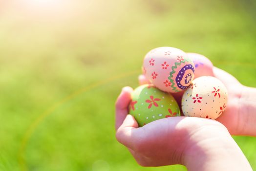 Happy easter! Close up of little kid holding colorful Easter eggs on green grass field background.