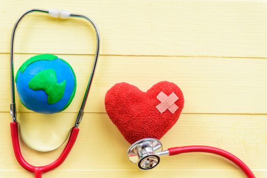 World health day, Healthcare and medical concept. Red heart with Stethoscope and handmade globe on Pastel white and yellow wooden background.