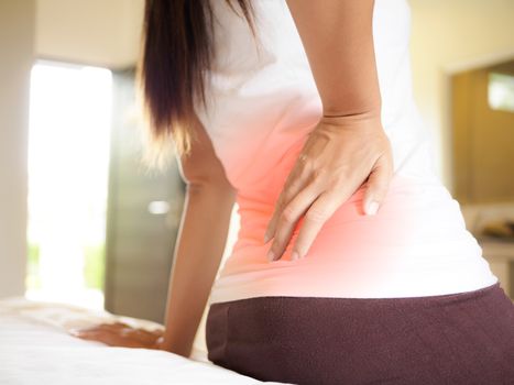 Young woman feeling pain in her back on the bed at home. Healthcare and medical concept.