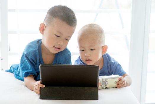 Young children addicted to technology gadget. Asian boys playing with digital tablet pc at home.