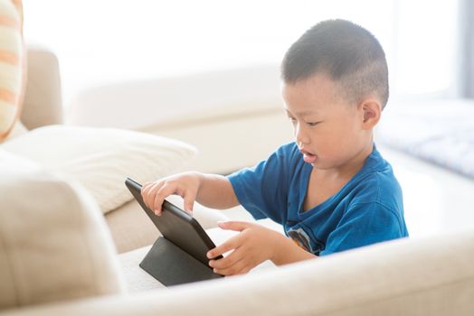 Young child addicted to technology gadget. Asian boy using digital tablet pc at home.