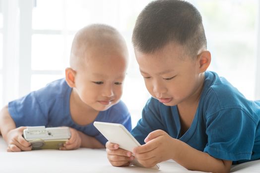 Young children addicted to technology gadget. Asian boys using smartphone at home.