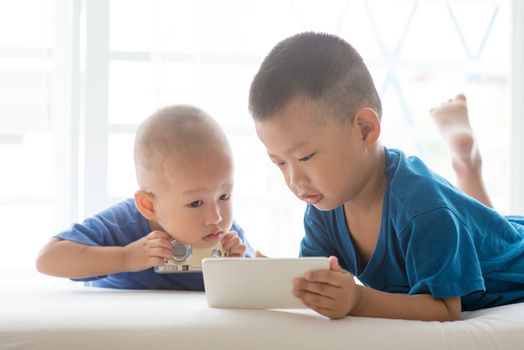 Young children addicted to technology gadget. Asian boys using smart phone at home.