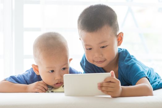 Young children addicted to technology gadget. Asian boys playing with smart phone at home.