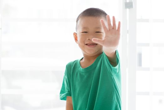 Young child at home. Playful Asian boy showing palm and giving high five.