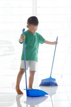 Young child doing house chores at home. Asian boy sweeping floor with broom.