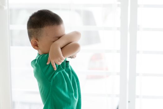 Young child at home. Playful Asian boy covering his face.