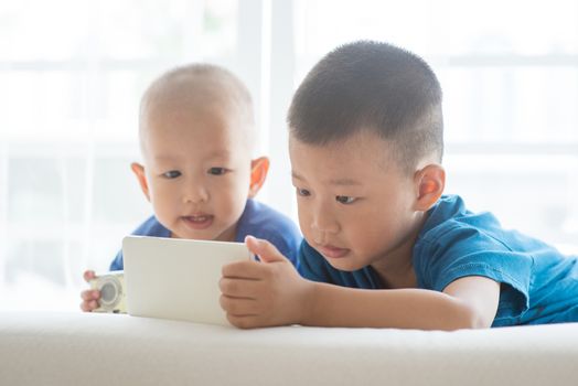 Young children addicted to technology gadget. Asian boys playing game with smart phone at home.