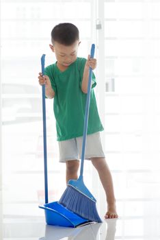 Asian boy sweeping floor with broom. Young child doing house chores at home.
