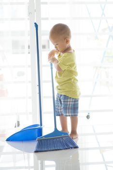 Young child doing house chores at home. Asian baby boy sweeping floor with broom.