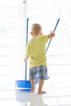 Young child doing house chores at home. Asian toddler sweeping floor with broom.