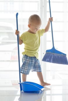 Asian baby boy sweeping floor with broom. Young child doing house chores at home.