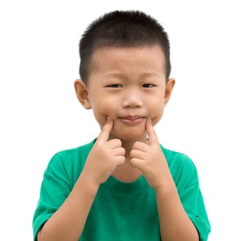 Happy Asian child pointing his cheeks and smiling. Portrait of young boy showing body parts isolated on white background.