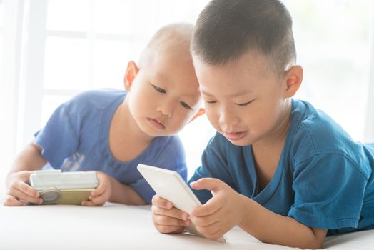Young children addicted to technology gadget. Asian boys playing with smartphone at home.
