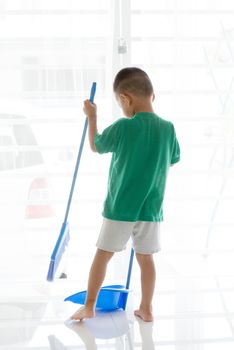 Young child doing house chores at home. Asian boy sweeping floor.