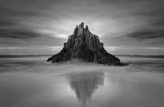 Moody sky over Pyramid Rock sea stack with tidal reflection.  Black and white