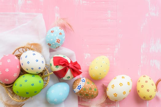 Happy easter! Colorful of Easter eggs tied with red ribbon in nest with paper star, flower and Feather on pastel color bright pink and white wooden background.