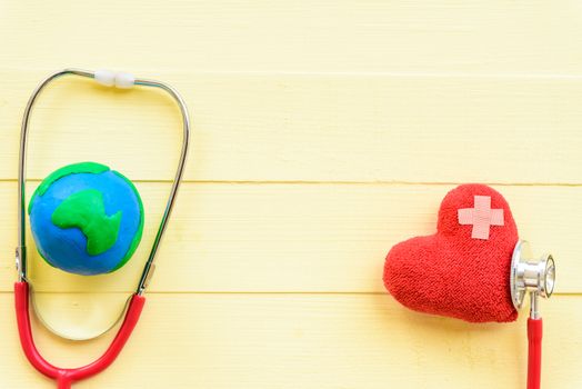 World health day, Healthcare and medical concept. Red heart with Stethoscope and handmade globe on Pastel white and yellow wooden background.