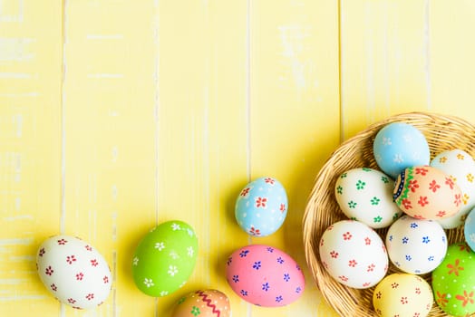 Happy easter! Colorful of Easter eggs in nest with red ribbon, Feather and paper star on pastel color bright yellow and white wooden background.