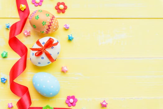 Happy easter! Colorful of Easter eggs in nest with red ribbon, Feather and paper star on pastel color bright yellow and white wooden background.