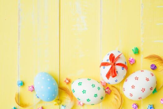 Happy easter! Colorful of Easter eggs in nest with red ribbon, Feather and paper star on pastel color bright yellow and white wooden background.