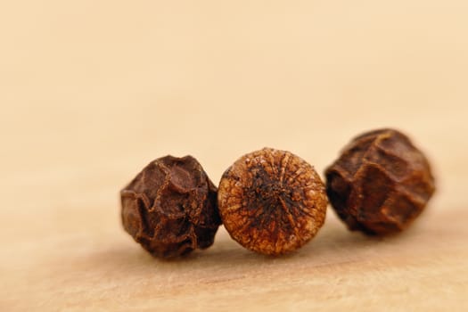 three black pepper seeds (Piper nigrum) on the wooden surface