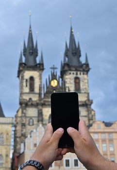 Close up man hands with smartphone taking picture of old town cityscape with Cathedral of Our Lady before Tyn, Prague, Czech Republic