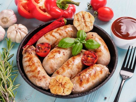 Chicken homemade sausages, sauces ketchup and vegetables and herbs on blue wooden background. Grilled sausages and grilled vegetables in black iron pan