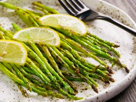 Close up view of grilled asparagus and slice of lemon in craft trendy plate on brown wooden table