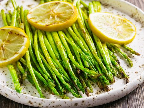 Close up view of grilled asparagus and slice of lemon in craft trendy plate on brown wooden table