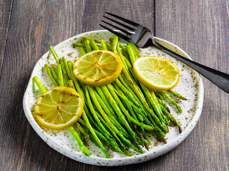 Close up view of grilled asparagus and slice of lemon in craft trendy plate on brown wooden table