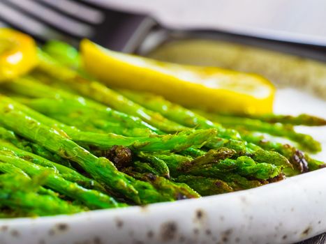 Close up view of grilled asparagus and slice of lemon in craft trendy plate on brown wooden table