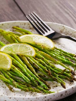 Close up view of grilled asparagus and slice of lemon in craft trendy plate on brown wooden table
