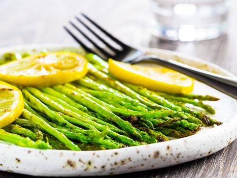 Close up view of grilled asparagus and slice of lemon in craft trendy plate on brown wooden table