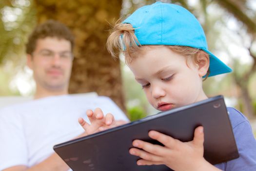 An infant child with food around his mouth is working, playing with tablet outdoors.