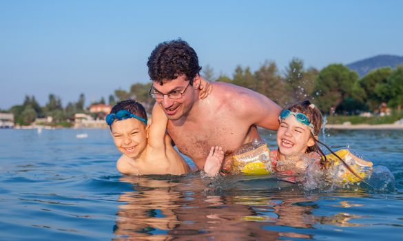 Young father having fun in sea waters during vacation in a hot summer day with his son and daughter.