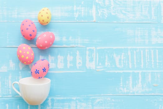 Happy easter! Row colorful Easter eggs spread out from white cup on bright green wooden background.