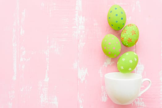 Happy easter! Row colorful Easter eggs spread out from white cup on bright pink and green wooden background.