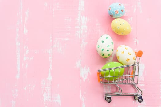 Happy easter! Row colorful Easter eggs spread out from shopping cart on bright pink wooden background.