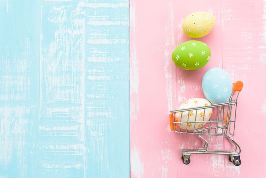 Happy easter! Row colorful Easter eggs spread out from shopping cart on bright pink and green wooden background.