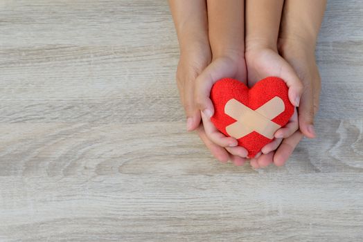 Health care, love, organ donation, family insurance and CSR concept. adult and child hands holding handmade red heart on wooden background.