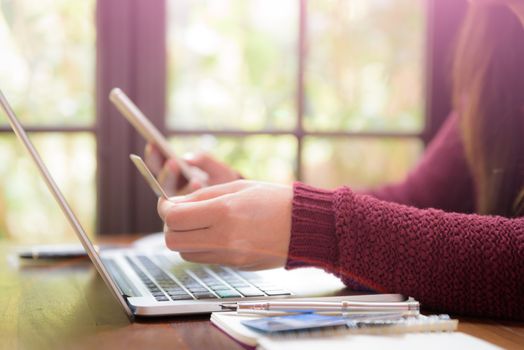 Pretty Young womans hands holding a credit card and using laptop computer for online shopping. Online payment. Female working on laptop in a cafe. Note book, pen and credit card put on table.