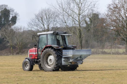 Red tractor with automatic lime spreader that sprinkles on a meadow in the early spring in the hamlet called Achterhoek in the East of the Netherlands.
