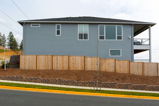 New garden wood fence with barkdust mulch and stone retaining wall around house in suburban neighborhood